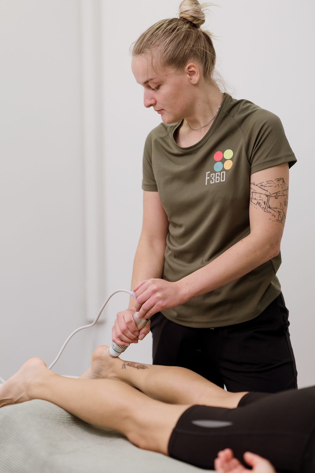 Lökéshullám-kezelés a lábszáron, a terapeuta az F360 pólójában